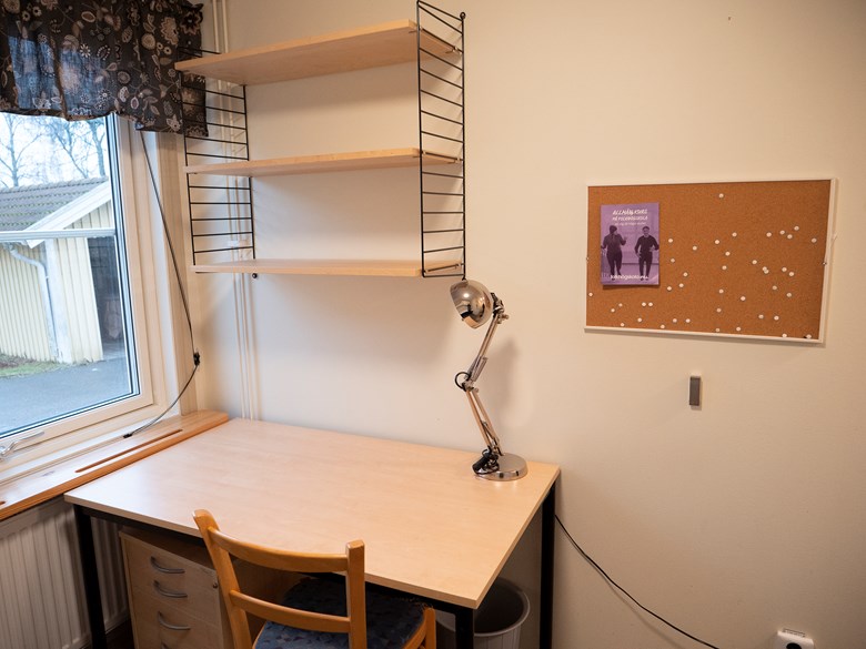 Litet enkelrum, Gråbo, Dalslands folkhögskola i Färgelanda. Ett skrivbord och stol med en hylla ovanför.