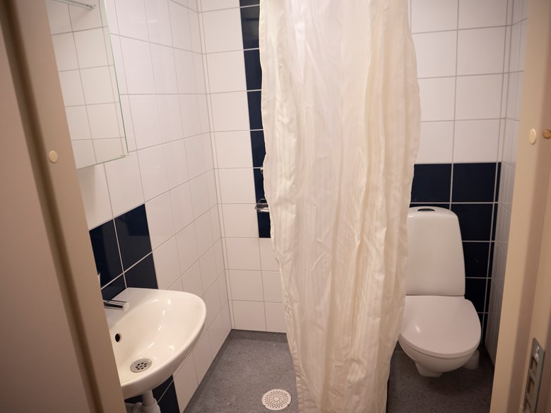Badrummet i litet enkelrum, Gråbo. Toalettstol, dusch och handfat med spegel.