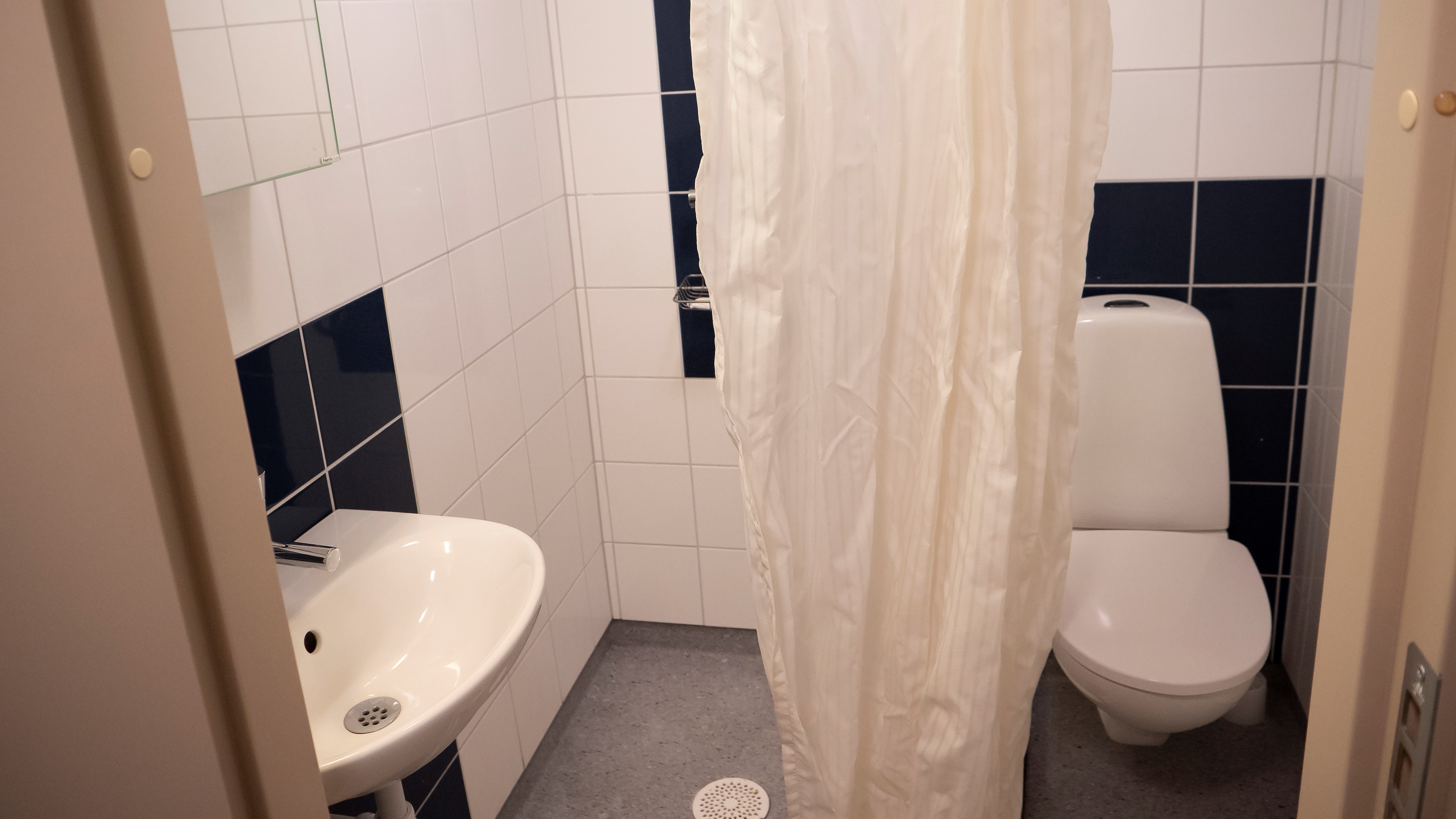 Badrummet i litet enkelrum, Gråbo. Toalettstol, dusch och handfat med spegel.