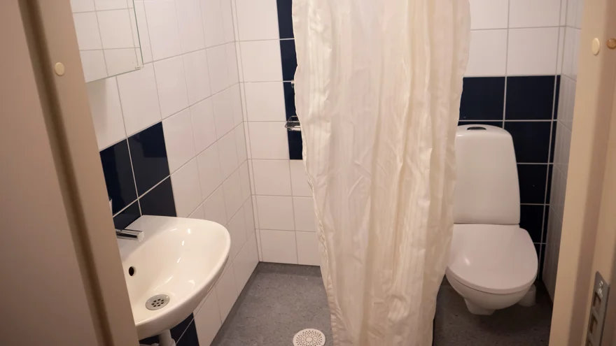 Badrummet i litet enkelrum, Gråbo. Toalettstol, dusch och handfat med spegel.