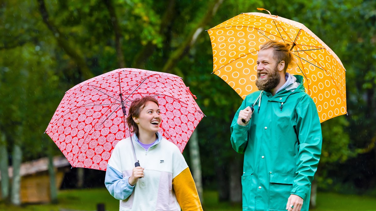 Två glada folkhögskoledeltagare som promenerar med paraplyer i regnet.