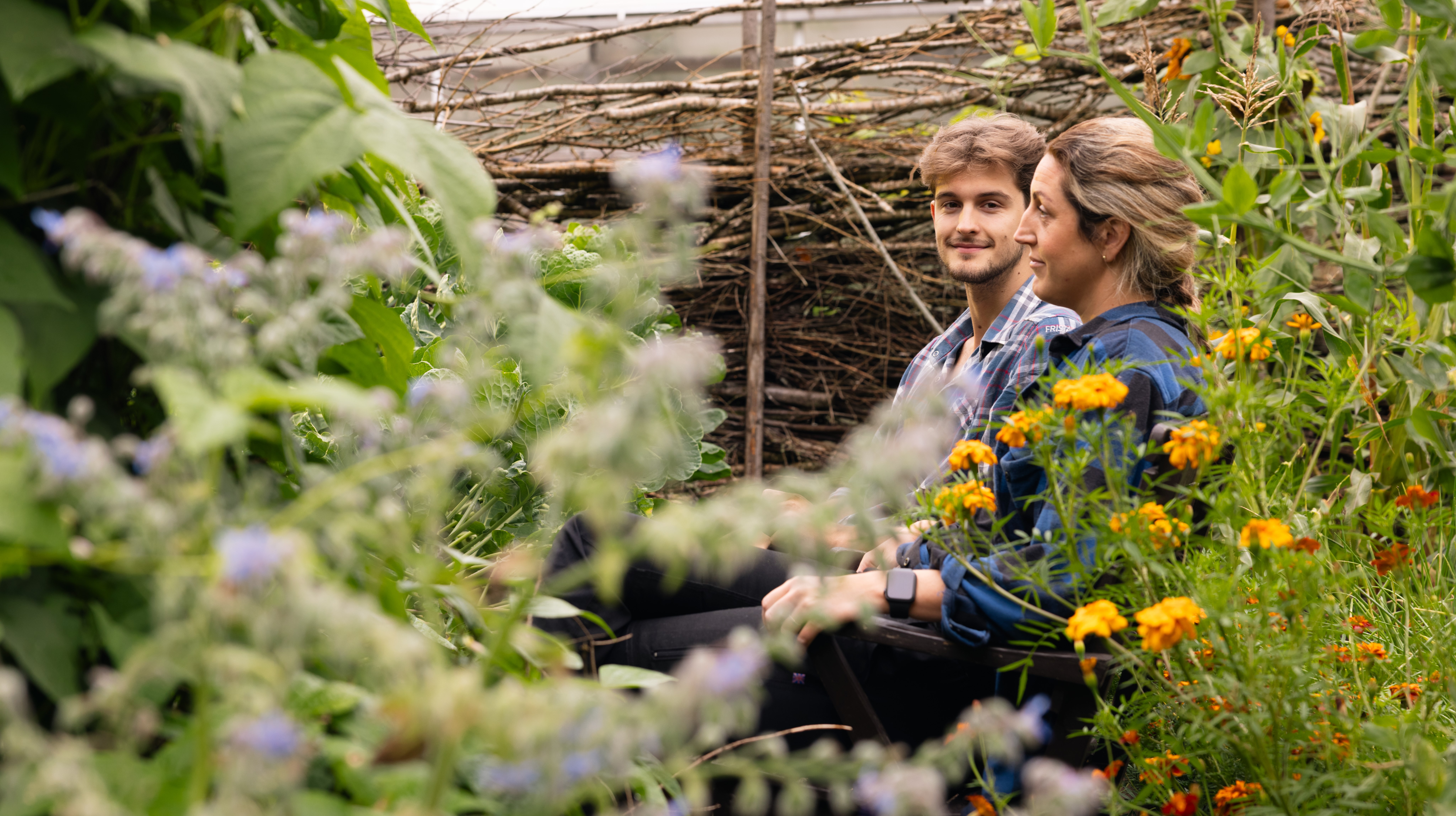 Två personer som sitter i en trädgård fylld av växter.