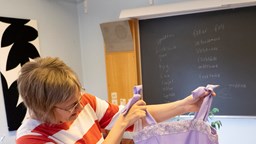 En lärare på folkhögskolan håller upp en lila klänning med vit spets.