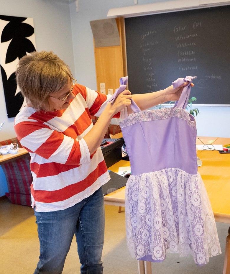 En lärare på folkhögskolan håller upp en lila klänning med vit spets.