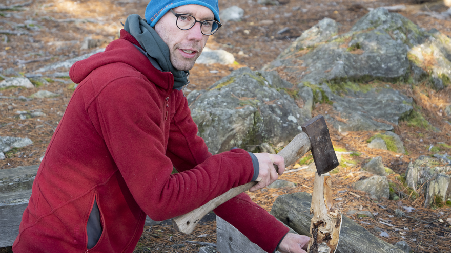 En man håller i ett vedträ och en yxa.