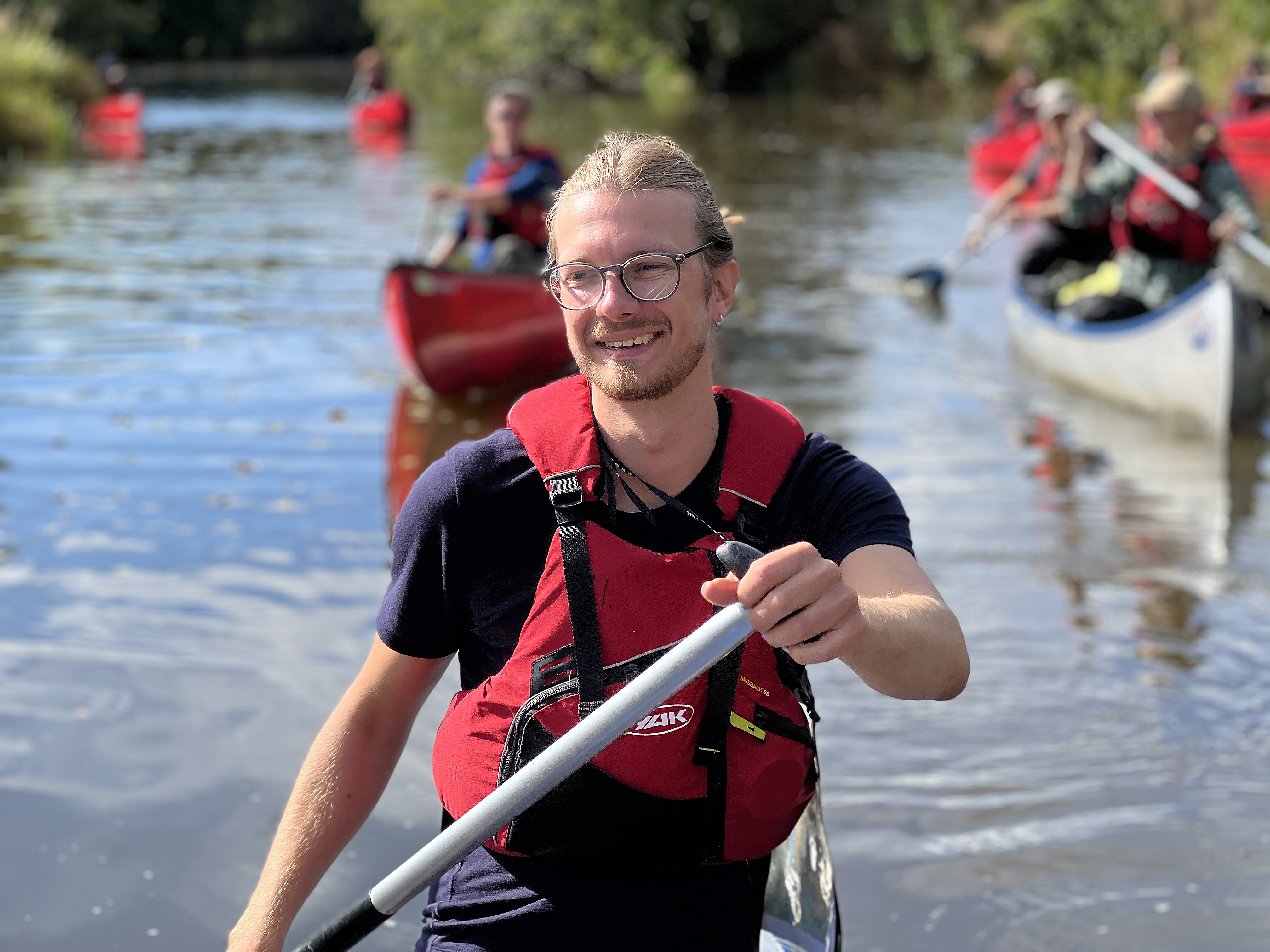 En person som paddlar kanadensare. I bakgrunden syns fler som paddlar.