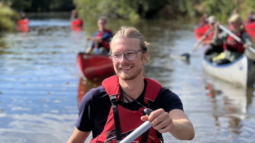 En person som paddlar kanadensare. I bakgrunden syns fler som paddlar.
