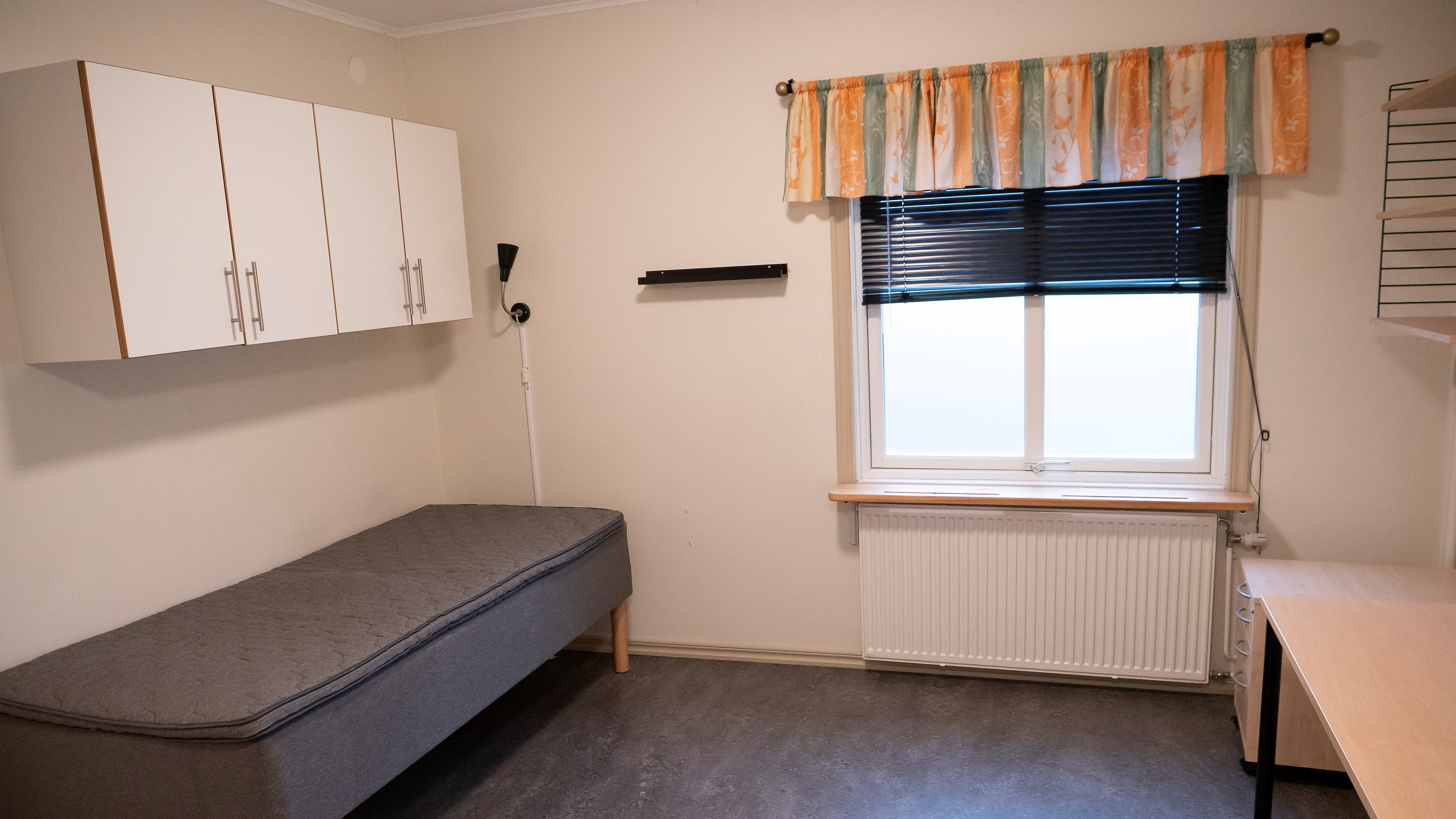 Stort enkelrum Gråbo, Dalslands folkhögskola i Färgelanda. Säng med skåp över till vänster och ett skrivbord, ett fönster och en hylla till höger.