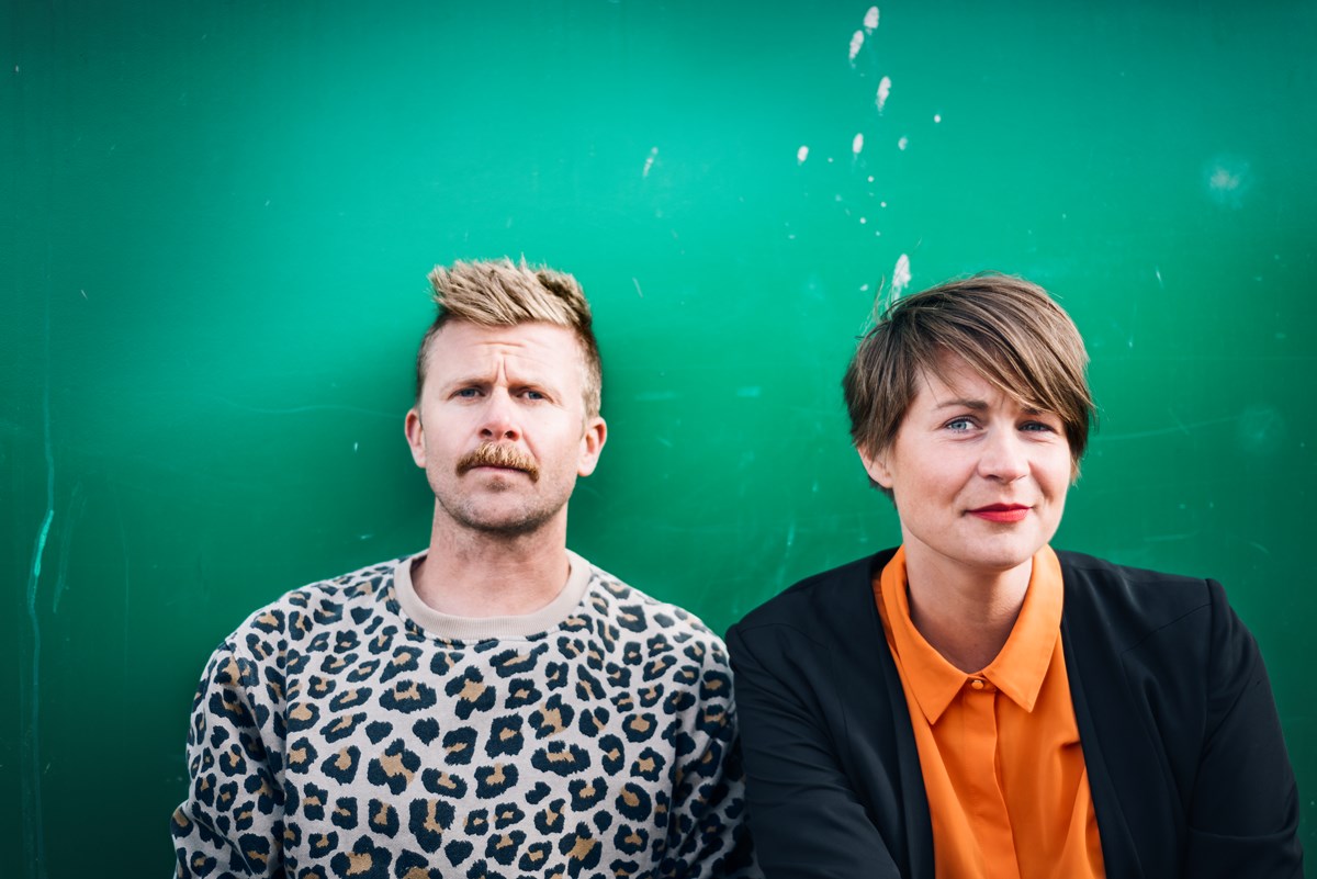 Linus Torgeby och Åsa Ekman framför en grön bakgrund. Båda tittar in i kameran. Linus har en leopardmönstrad tröja på sig och Åsa bär en orange skjorta samt svart kavaj. 