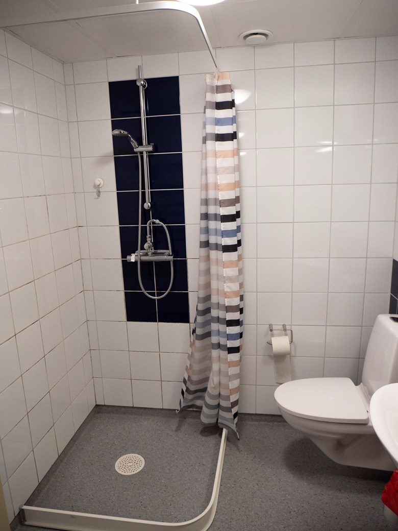 Dusch med duschdraperi och en toalettstol.