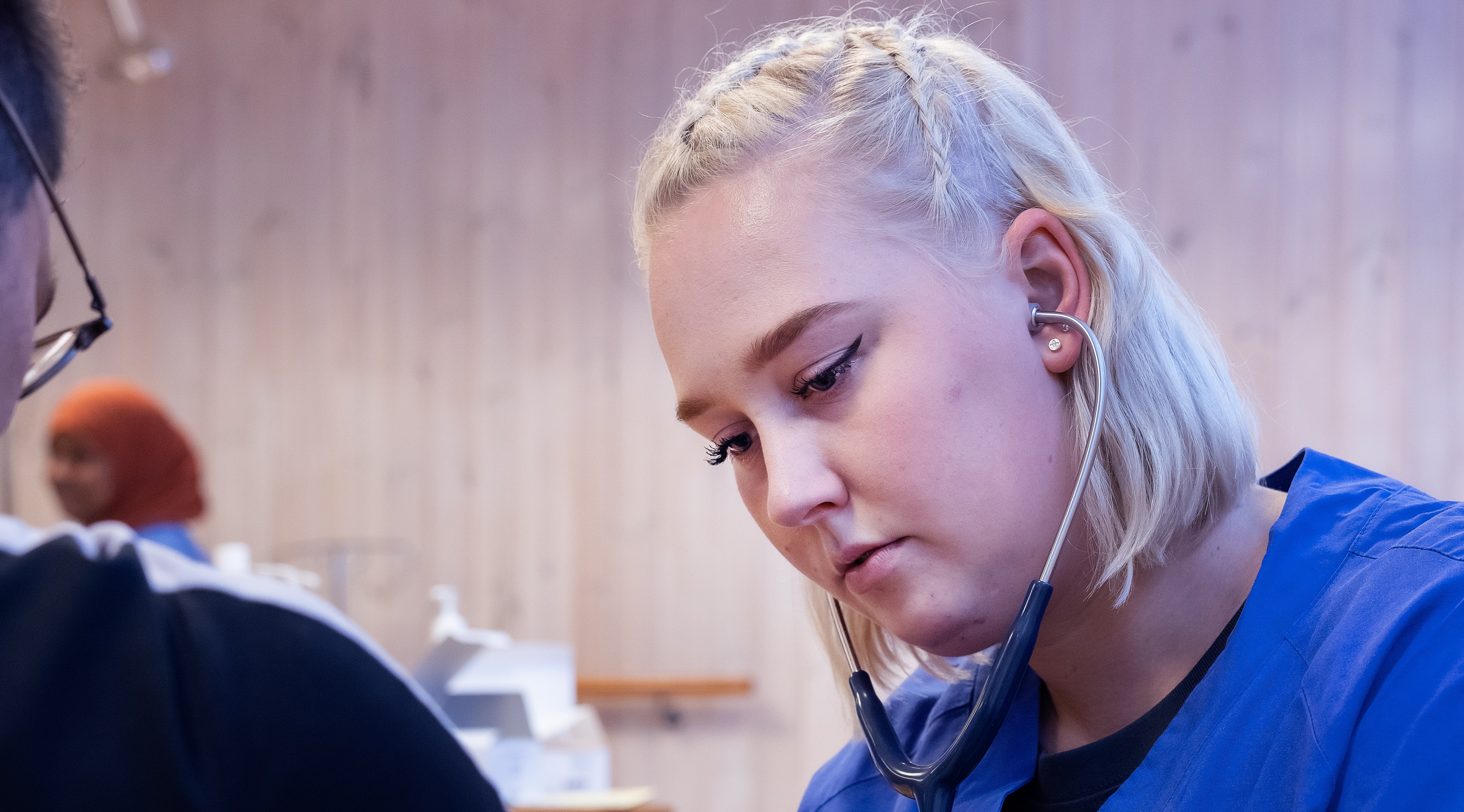 En folkhögskoledeltagare som läser till undersköterska som hjälper en sittande person.