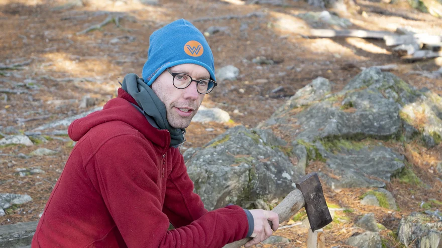 En man håller i ett vedträ och en yxa.