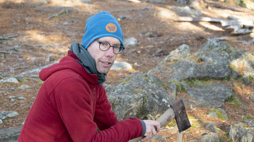 En man håller i ett vedträ och en yxa.