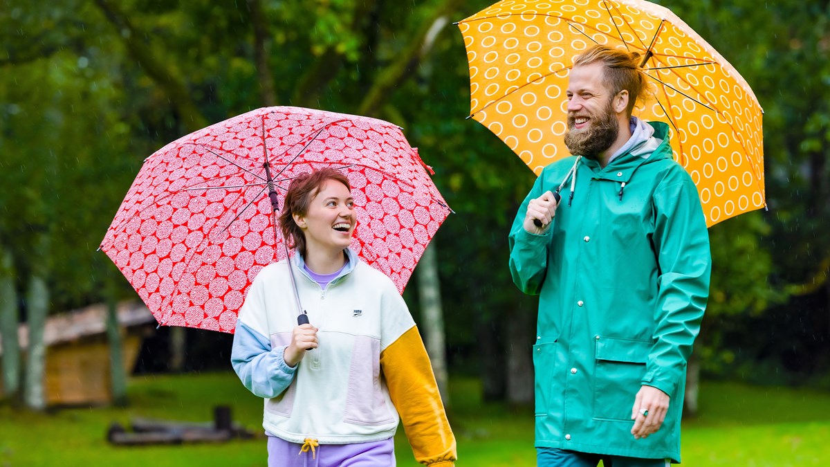 Två folkhögskoledeltagare som ler och promenerar i regnet med paraplyer.