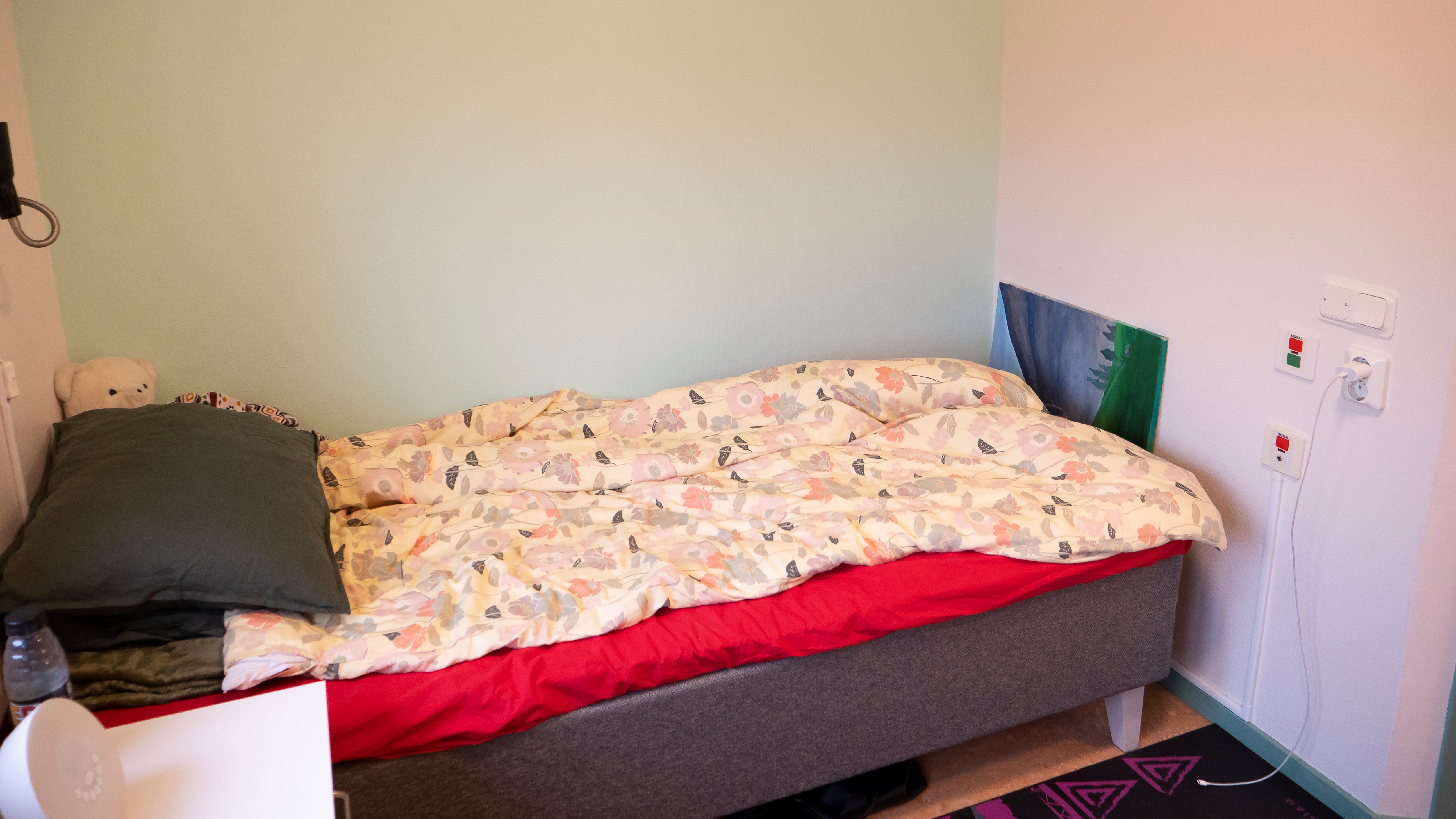 En säng framför en mintgrön fondvägg.