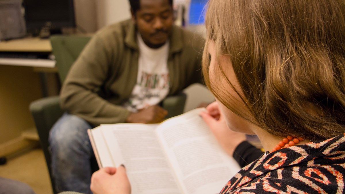 En folkhögskoledeltagare som läser i en bok. I bakgrunden syns en annan folkhögskoledeltagare.