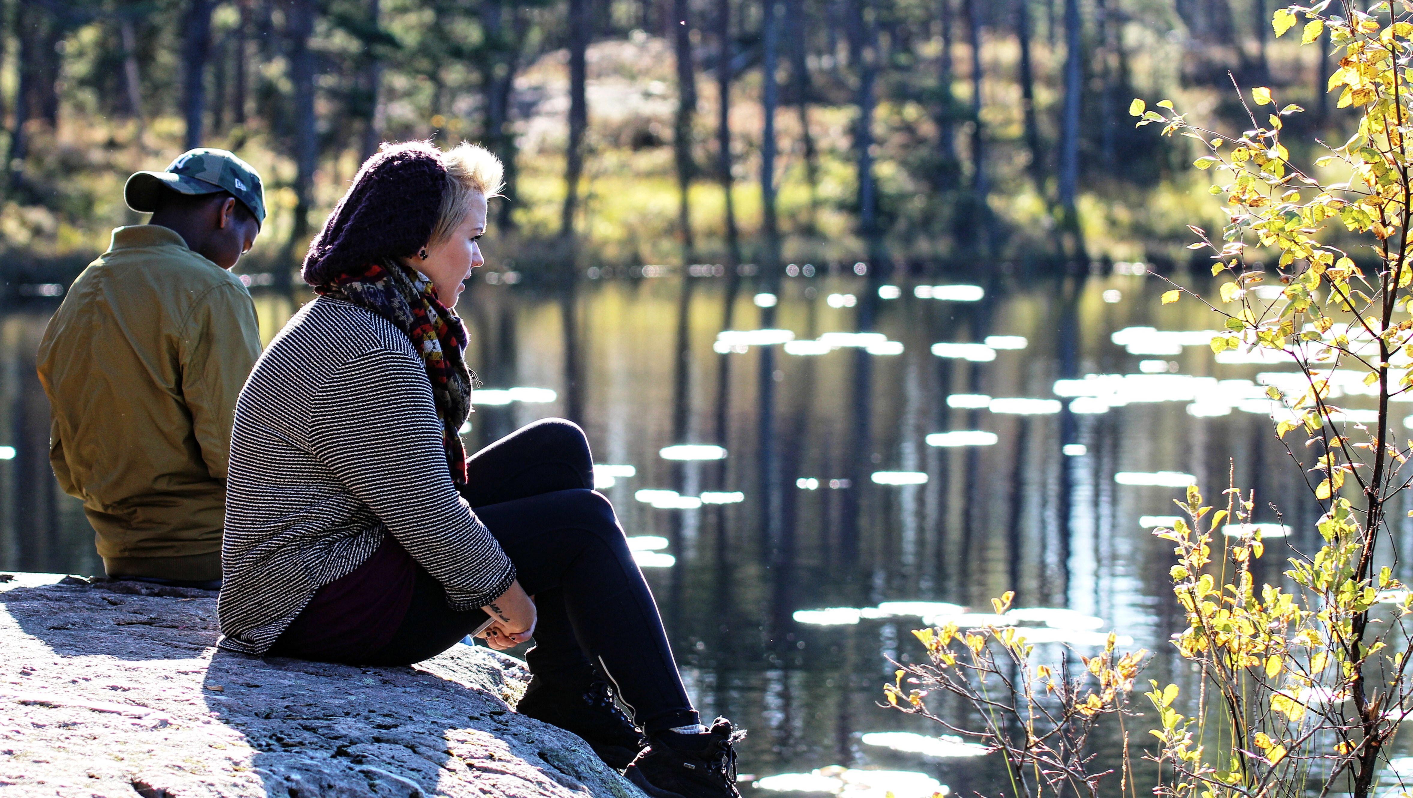 Två folkhögskoledeltagare på Livslinjen. De sitter på en klipphäll vid en skogstjärn. Solen skiner.