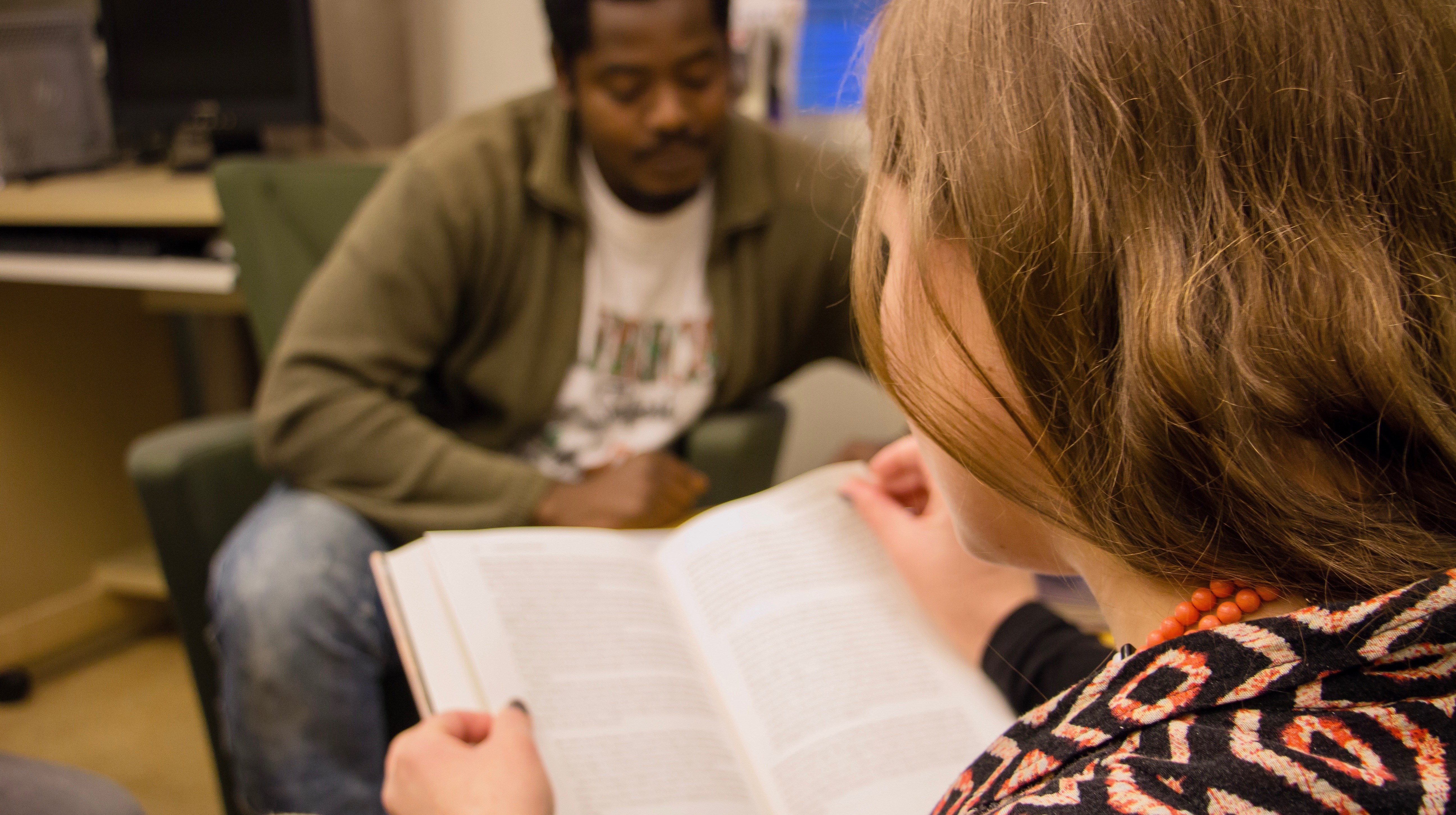 Bilden visar en folkhögskoledeltagare som läser. I bakgrunden syns en annan folkhögskoledeltagare som blickar ner mot sitt arbete.