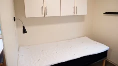 Litet enkelrum, Gråbo, Dalslands folkhögskola. En säng med sänglampa och fyra skåp ovanför.