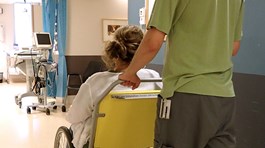 En person som transporterar en kvinna i rullstol på ett sjukhus