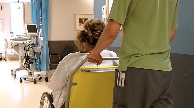 En person som transporterar en kvinna i rullstol på ett sjukhus