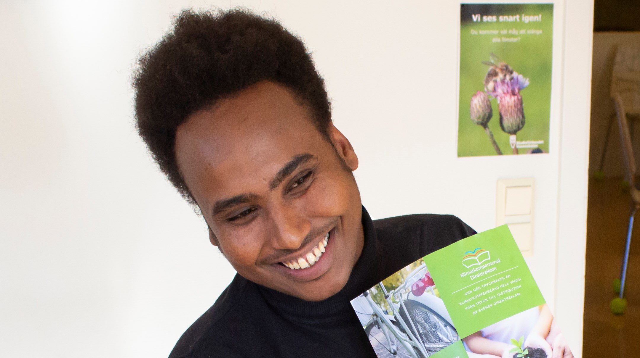 Faraah Mohamud, som är projektledare på Västra Vi Unga, på sin arbetsplats där han håller upp en broschyr.