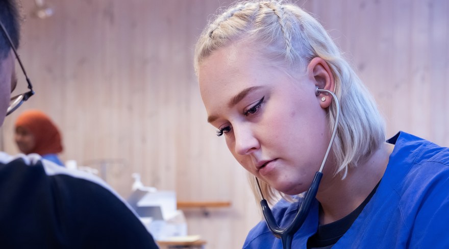 En folkhögskoledeltagare som läser till undersköterska som hjälper en sittande person.