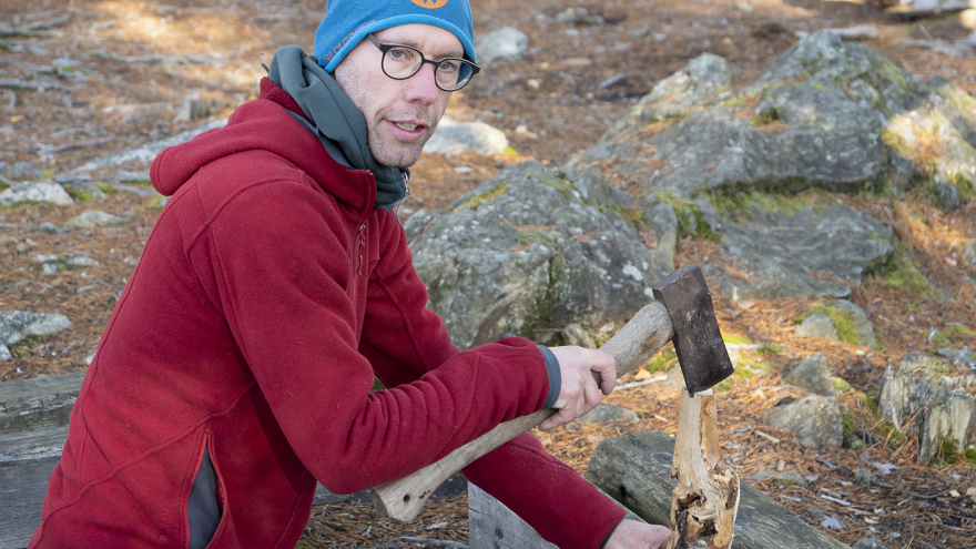 En man håller i ett vedträ och en yxa.